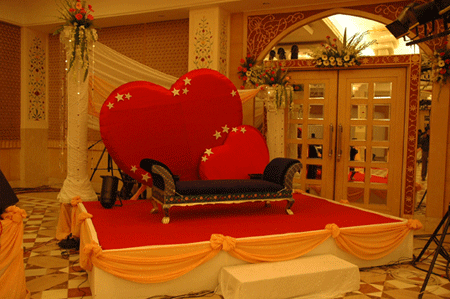 Pretty little stage with two red colored heart behind the bride groom sitting couch